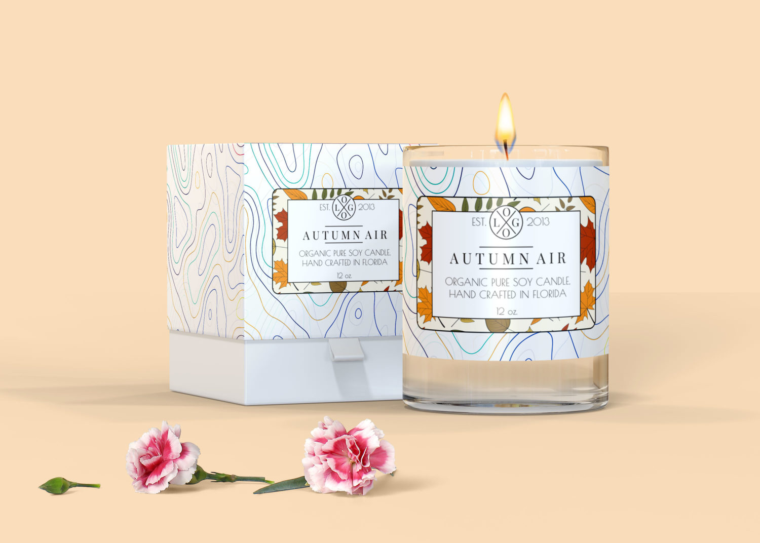A clear glass candle labeled "Autumn Air" sits beside a patterned box, with pink flowers on a soft, beige surface.