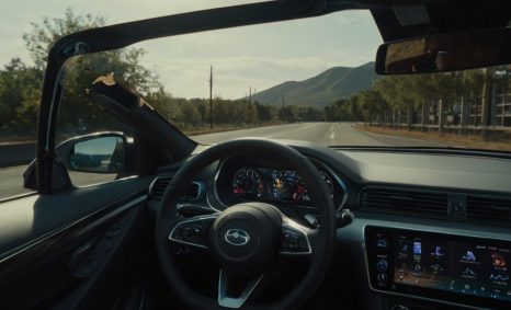 A view from the driver's seat of a car, showing a winding road with mountains in the background and a clear sky.